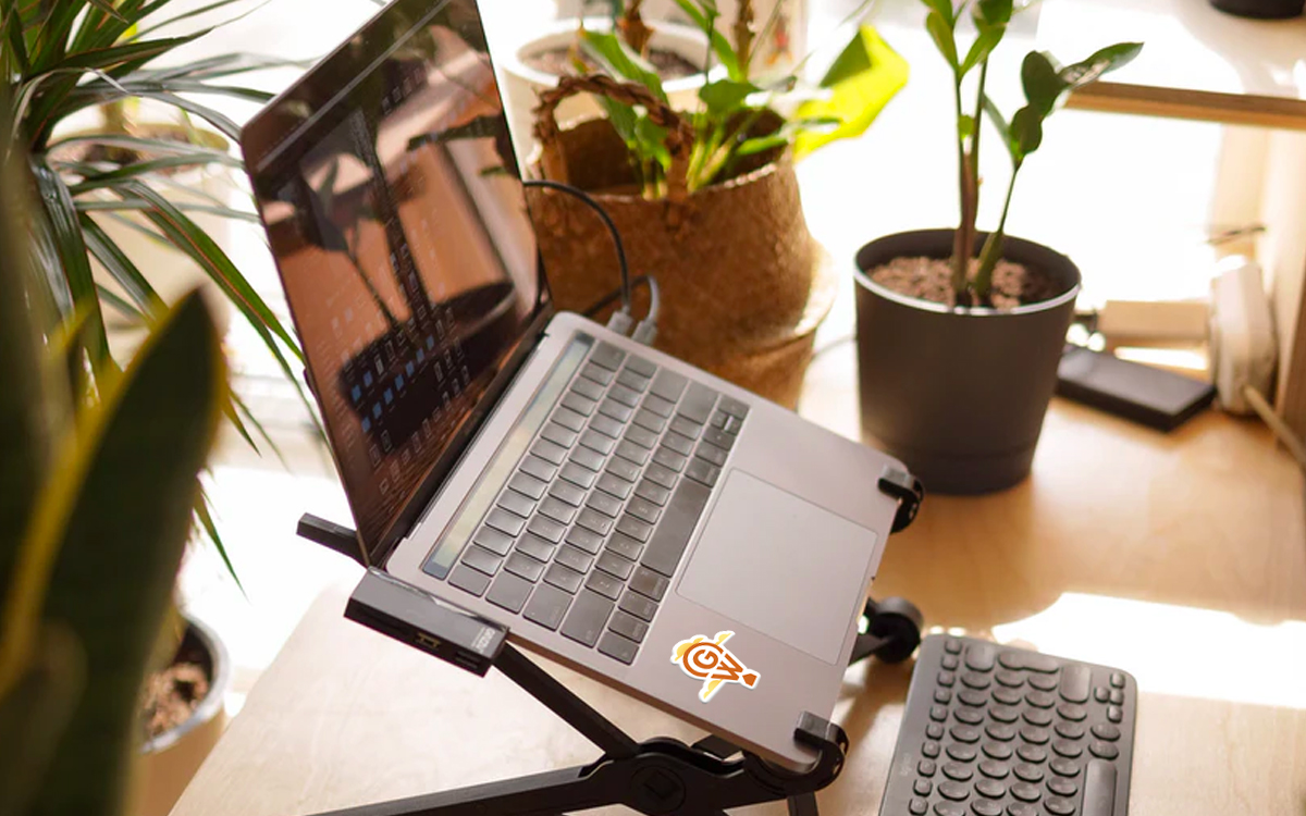 Laptop opened on desk surrounded with plants with GroundWork sticker.